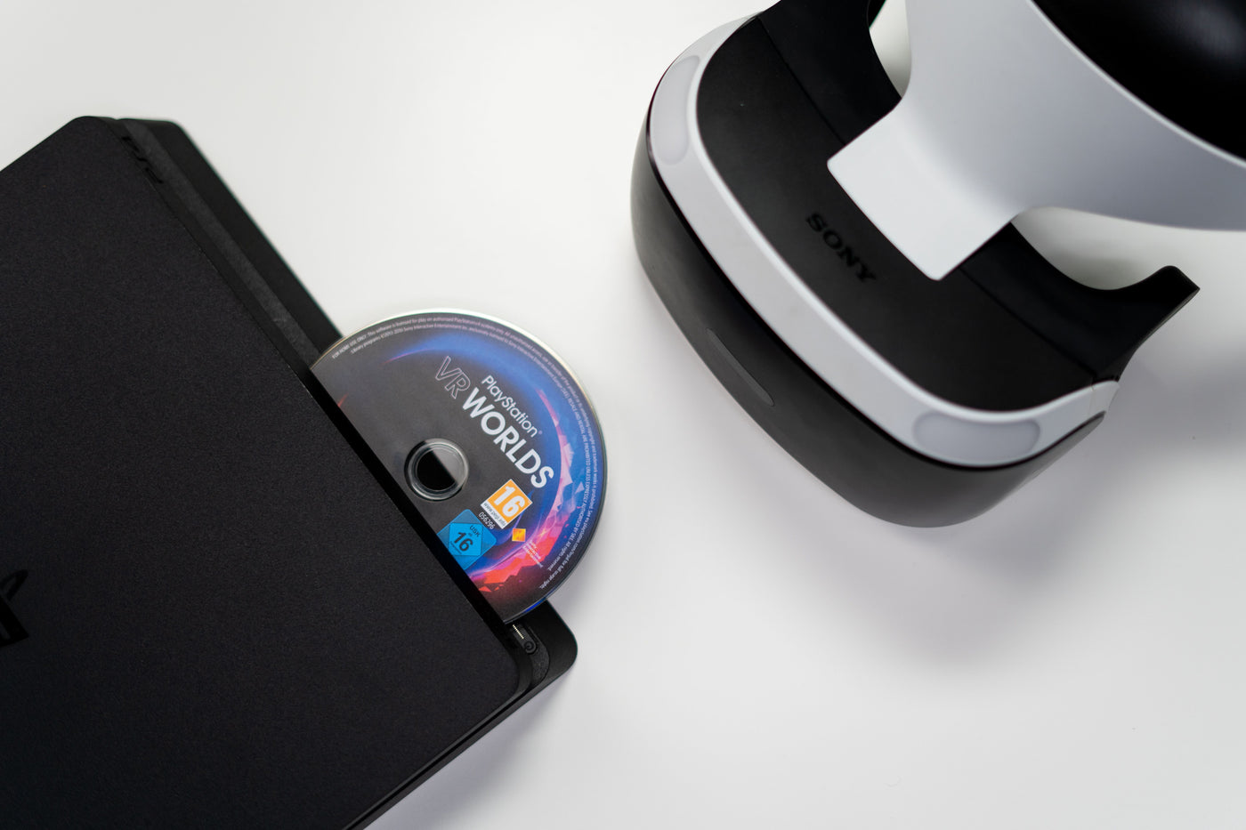 Disco de jogo PlayStation a ser inserido numa consola, ao lado de um headset PlayStation VR
