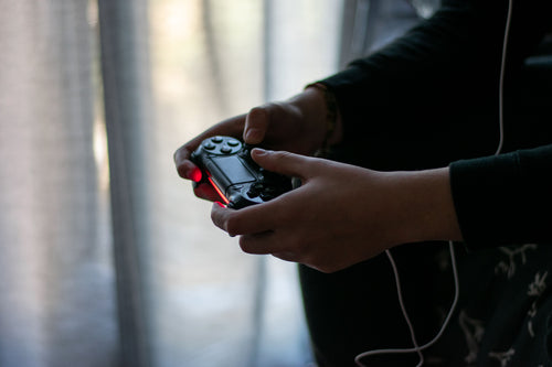 Mãos a segurar um comando de videojogos numa sala escura, simbolizando as horas passadas a jogar videojogos