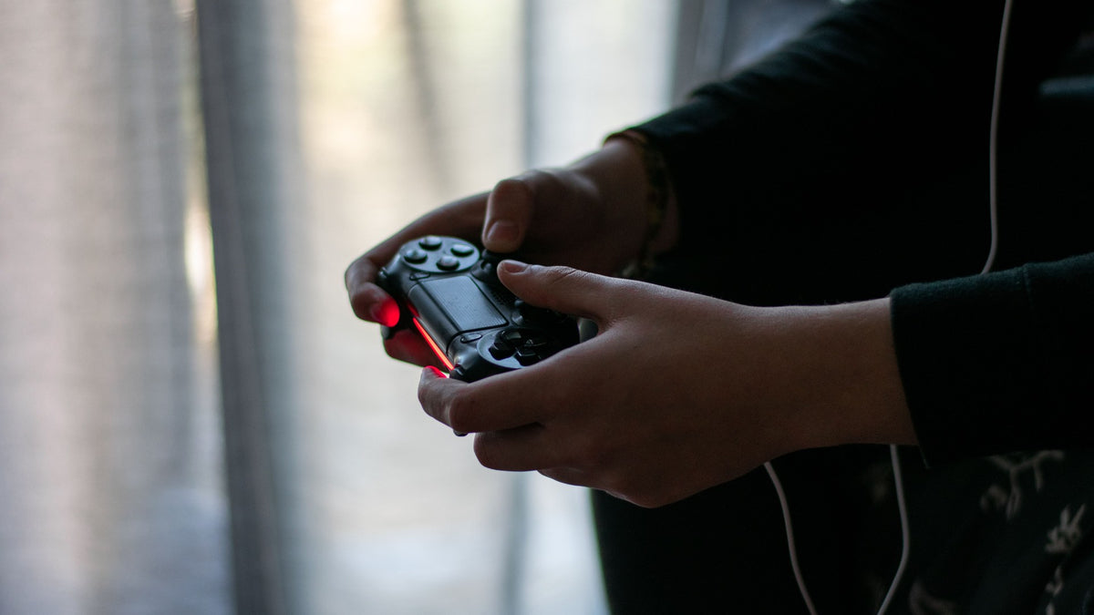Mãos a segurar um comando de videojogos numa sala escura, simbolizando as horas passadas a jogar videojogos