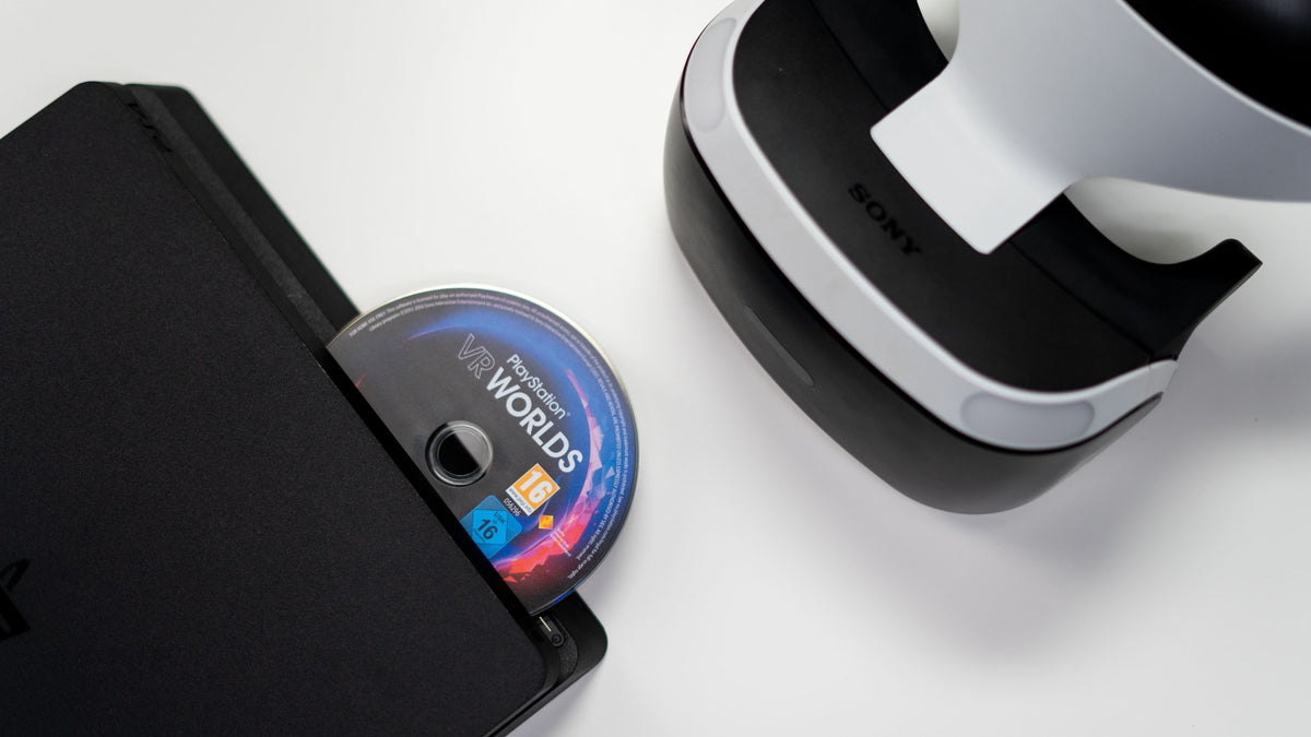 Disco de jogo PlayStation a ser inserido numa consola, ao lado de um headset PlayStation VR