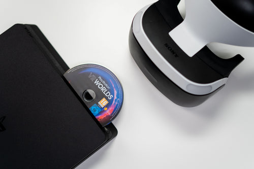 Disco de jogo PlayStation a ser inserido numa consola, ao lado de um headset PlayStation VR