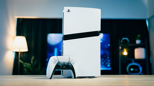 Consola PlayStation 5 e comando numa sala de estar acolhedora, com luz quente de candeeiro e o ecrã da televisão a brilhar a azul ao fundo